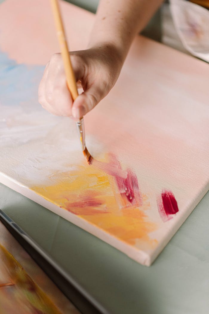Close-up of a hand painting vibrant colors on a canvas, highlighting artistic creativity and process.