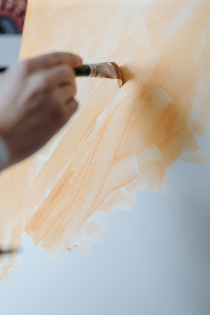 Close-up of an artist using a brush to paint soft strokes on a canvas with warm tones.